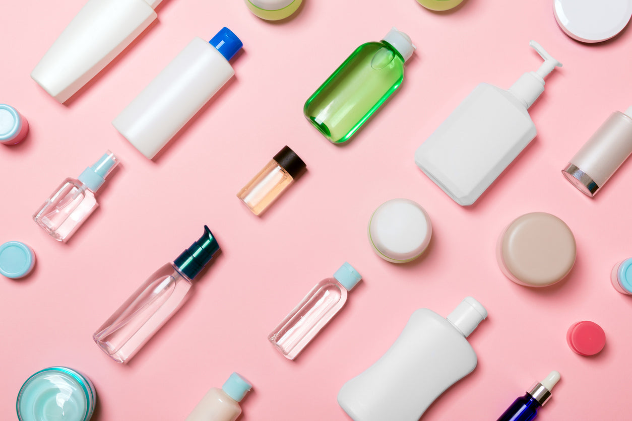 A picture of cosmetic bottles and containers lying on a pink background