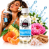 A bottle of Fizzy Whiz Agua Mística fragrance oil centered in front of a woman spraying a matching blue atomizer. The scene is styled with citrus fruits, a pink flower, water splash graphics, and salt crystals on a white background.