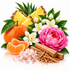 A styled arrangement of citrus and floral ingredients on a white background: pineapple slices, a whole orange, peeled orange segments, white blossoms, a large pink flower, green leaves, cinnamon sticks, and pink crystalline salt.