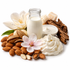 A glass bottle filled with white milk or almond milk, surrounded by almonds, a pink flower, a white blossom, whipped cream, and a dollop of thick yogurt on a clean white background.