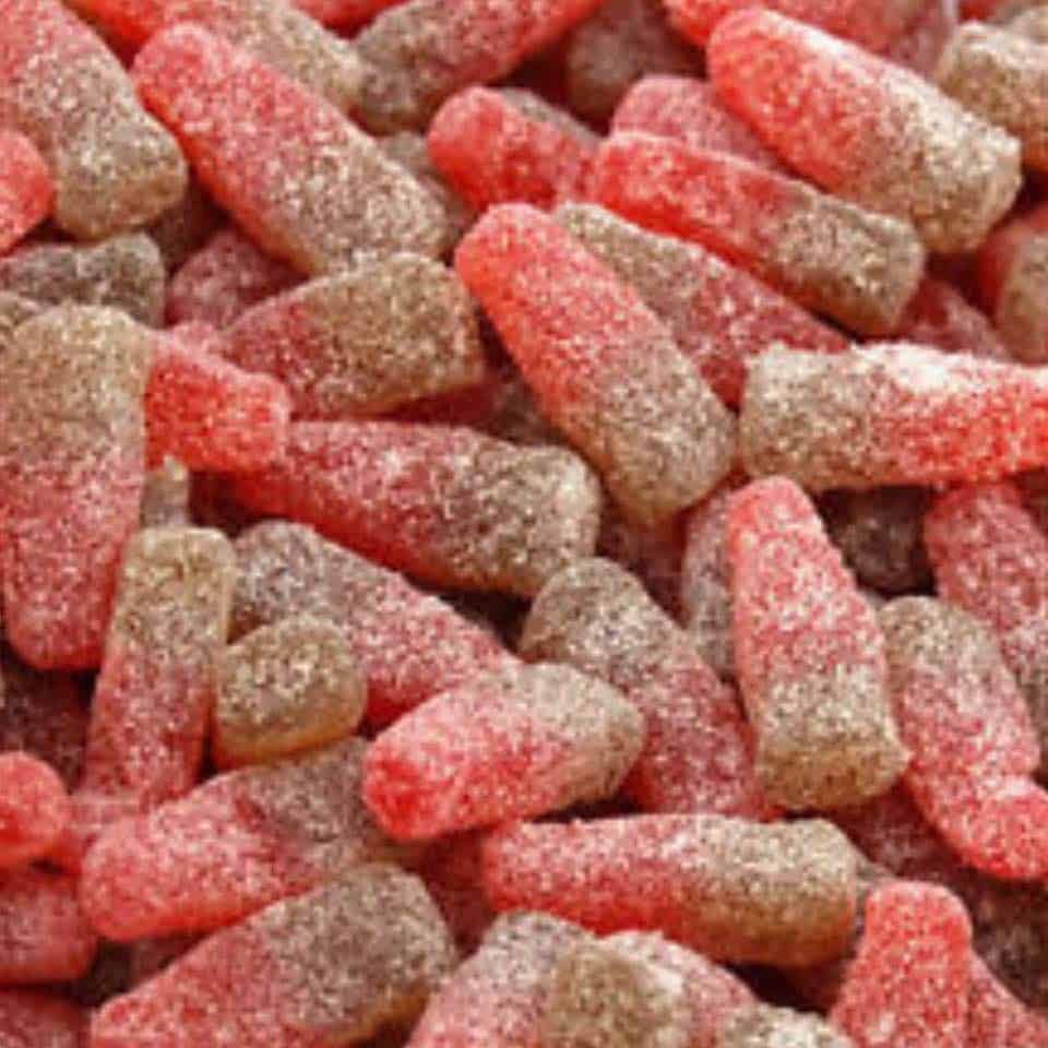 A close-up image of small, candy-like structures coated with a sugary glaze, with a cherry red color and a fizzy cola appearance.