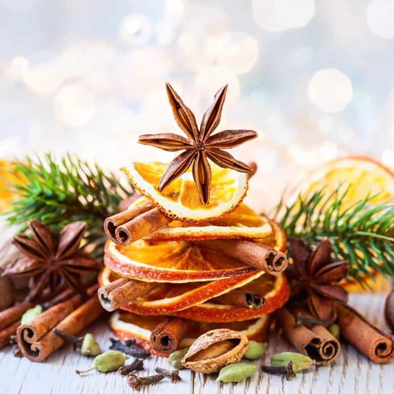 A Christmas spice fragrance oil product displayed with holiday-themed decorations, including dried orange slices, cinnamon sticks, and pine needles.