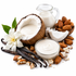 A styled studio arrangement of coconut milk and cream ingredients on a white background, including a halved coconut, a small glass pitcher of white liquid, a bowl of creamy product, whole and cracked almonds, vanilla beans, and a white flower.