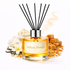Reed diffuser bottle labelled delicia drench with vanilla flowers and caramel candies on a white background