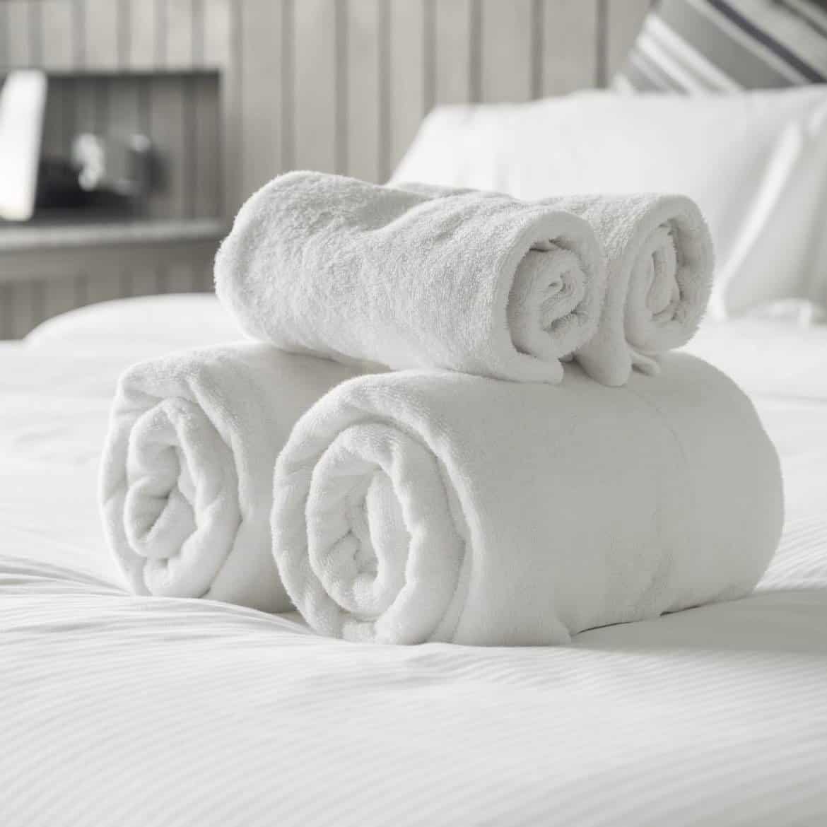 A stack of rolled-up white towels on a bed with a focus on the fresh, clean fragrance oil beside them.
