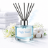 Diffuser with 'Fluffy Towels' label surrounded by white flowers and cotton on a light background