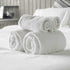 A stack of rolled-up white towels on a bed with a focus on the fresh, clean fragrance oil beside them.
