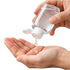 Hand pouring clear liquid from a small bottle into another hand on a white background