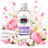 A clear bottle of Fizzy Whiz Heaven Scent Fragrance Oil with a white cap and white label, surrounded by pink peonies, white lilies, cotton bolls, folded white towels, and pink flower petals on a white background.