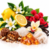 A styled product arrangement of assorted chocolates in the foreground, with amber crystals, vanilla beans, white orchids, lemon halves, raspberries, and green leaves arranged on a clean white background.