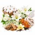 A styled spa-themed arrangement on a white background featuring a basket of cotton, folded white and beige towels, white lilies, small white blossoms, amber-colored stones, cinnamon sticks, vanilla beans, and wood pieces.