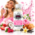 A bottle of Fizzy Whiz Marshmallow Boujee Fragrance Oil centered in front of a woman spraying perfume, with pink marshmallows, strawberries, raspberries, a coconut, caramel pieces, vanilla beans, flowers, and a pink splash graphic on a white background.