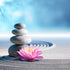 A stack of smooth stones in a Zen garden with a vibrant pink lotus flower in front, set against a blurred background of sandy textures and a blue sky.