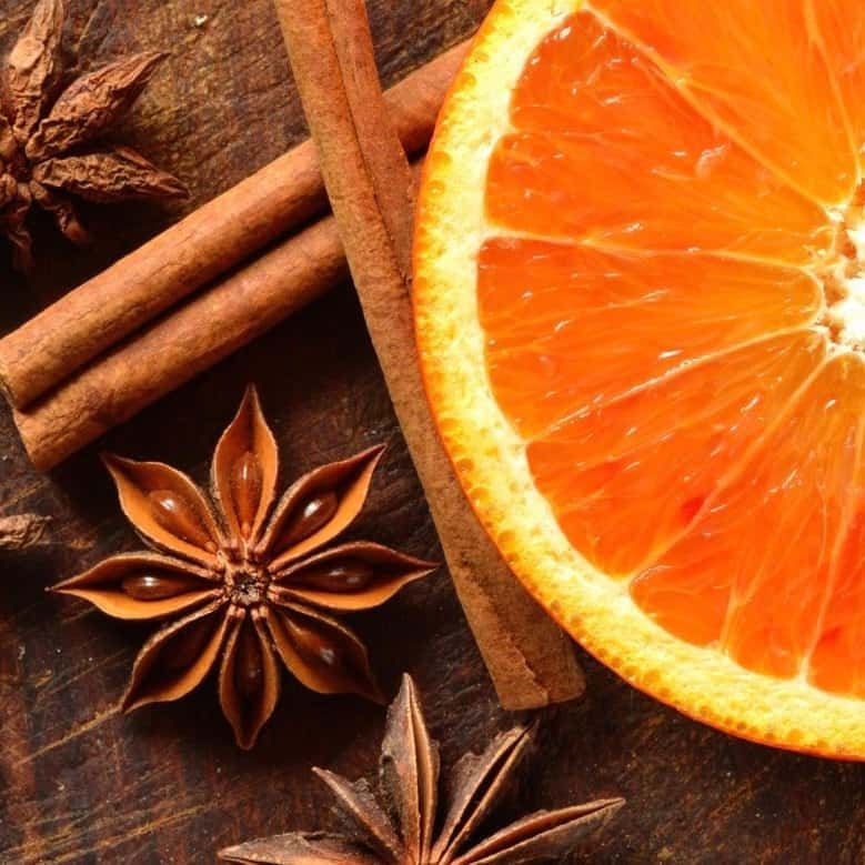 A close-up image of an orange slice and cinnamon sticks with star anise on a wooden surface.