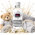 A bottle of Fizzy Whiz PJ Day fragrance oil centered on a white background, surrounded by baby-themed props including a teddy bear in striped pajamas, a star-patterned pillow, a folded striped blanket, a sleep mask, and small flowers. Cream-colored liquid splashes appear behind the bottle.