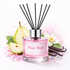 Pink diffuser bottle labeled 'Pixie Dust' with black sticks, pear slices, vanilla beans, and flowers on a white background.