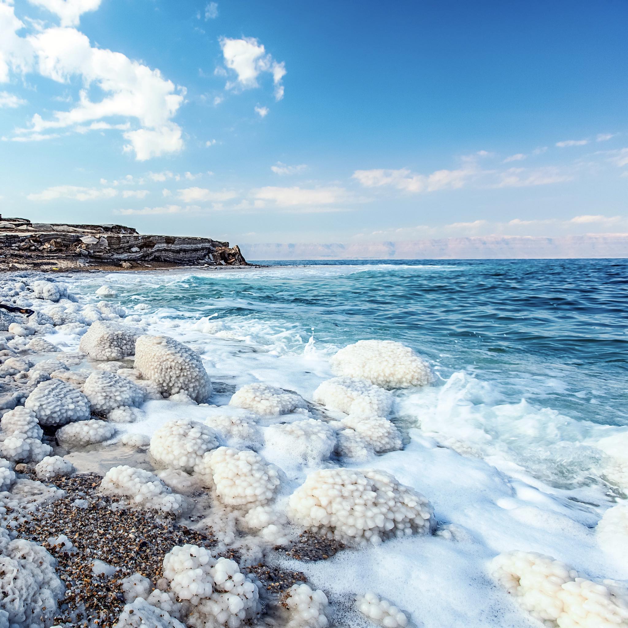 A scenic view of a salty beach with white crystals on the shore, where the ocean meets the sky with some clouds.