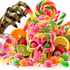 A vibrant and colorful Halloween-themed candy display featuring a skull-shaped jar filled with pink and green slime, gummy worms, and sprinkles, surrounded by an assortment of sweets, citrus slices, and a zombie hand on a white background.