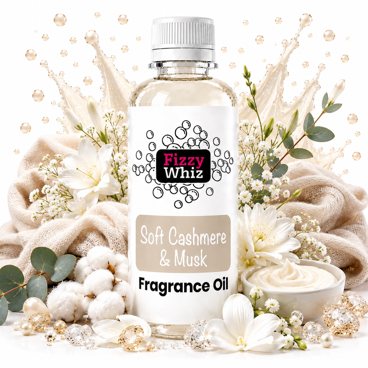 A bottle of Fizzy Whiz Soft Cashmere & Musk Fragrance Oil centered on a white background, surrounded by decorative props including cream-colored towels, white flowers, cotton bolls, green leaves, and a small bowl of creamy fragrance oil. The bottle has a white cap and a white label with black and pink branding.