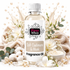 A bottle of Fizzy Whiz Soft Cashmere & Musk Fragrance Oil centered on a white background, surrounded by decorative props including cream-colored towels, white flowers, cotton bolls, green leaves, and a small bowl of creamy fragrance oil. The bottle has a white cap and a white label with black and pink branding.