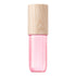 A pink translucent cosmetic bottle with a light natural wood grain cap, shown against a solid white background.