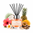 A reed diffuser bottle with black reeds, labeled 'Sol Cheeky Bikini,' surrounded by tropical fruit and flowers including pineapple, mango, passion fruit, hibiscus, plumeria, coconut, and ginger on a white background.