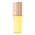 A small cylindrical cosmetic bottle with a light natural wood cap and a translucent yellow lower chamber, shown on a plain white background.