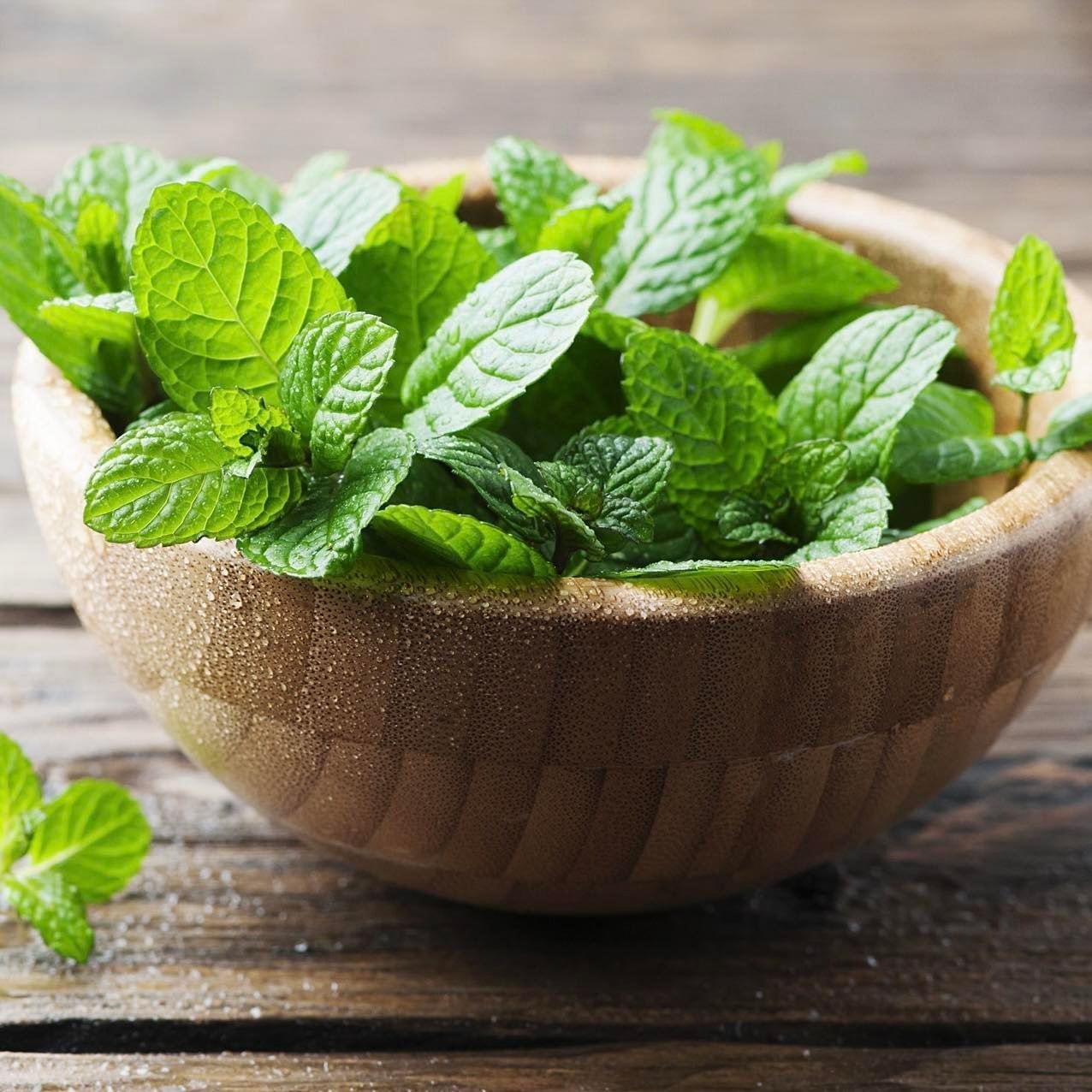 A wooden bowl filled with fresh spearmint leaves on a wooden surface.