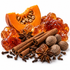 A styled arrangement of whole and sliced spices on a white background, including a halved orange pumpkin, amber-colored candied fruit pieces, cinnamon sticks, star anise, cloves, and nutmegs.
