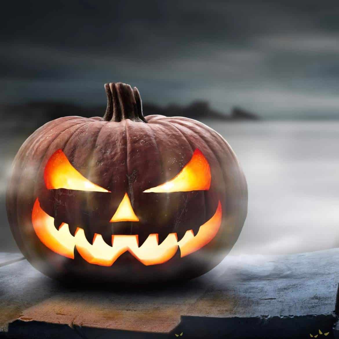 A carved pumpkin with a spooky face illuminated from the inside, set against a misty background.